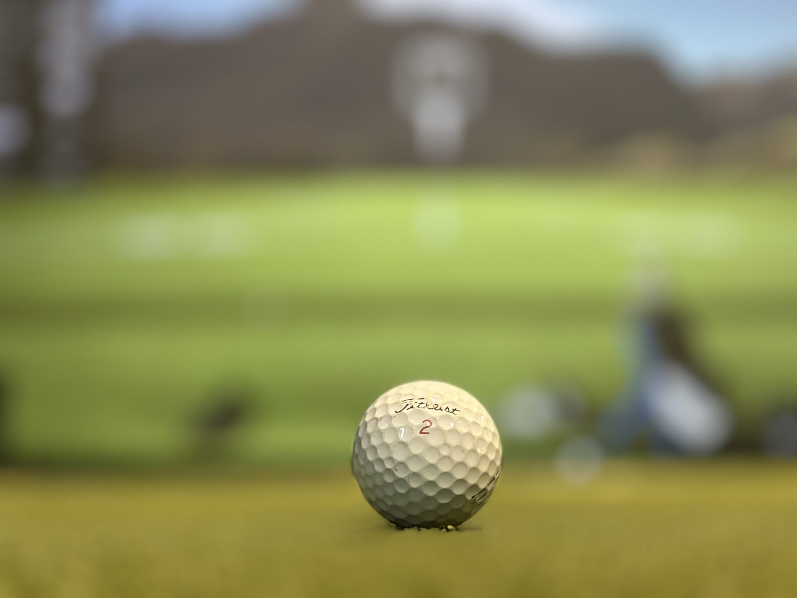 Close-up of a Titleist golf ball marked with the number 2 resting on grass, with a blurred golf course in the background—perfect for your next round after easy tee time booking with Tee24.