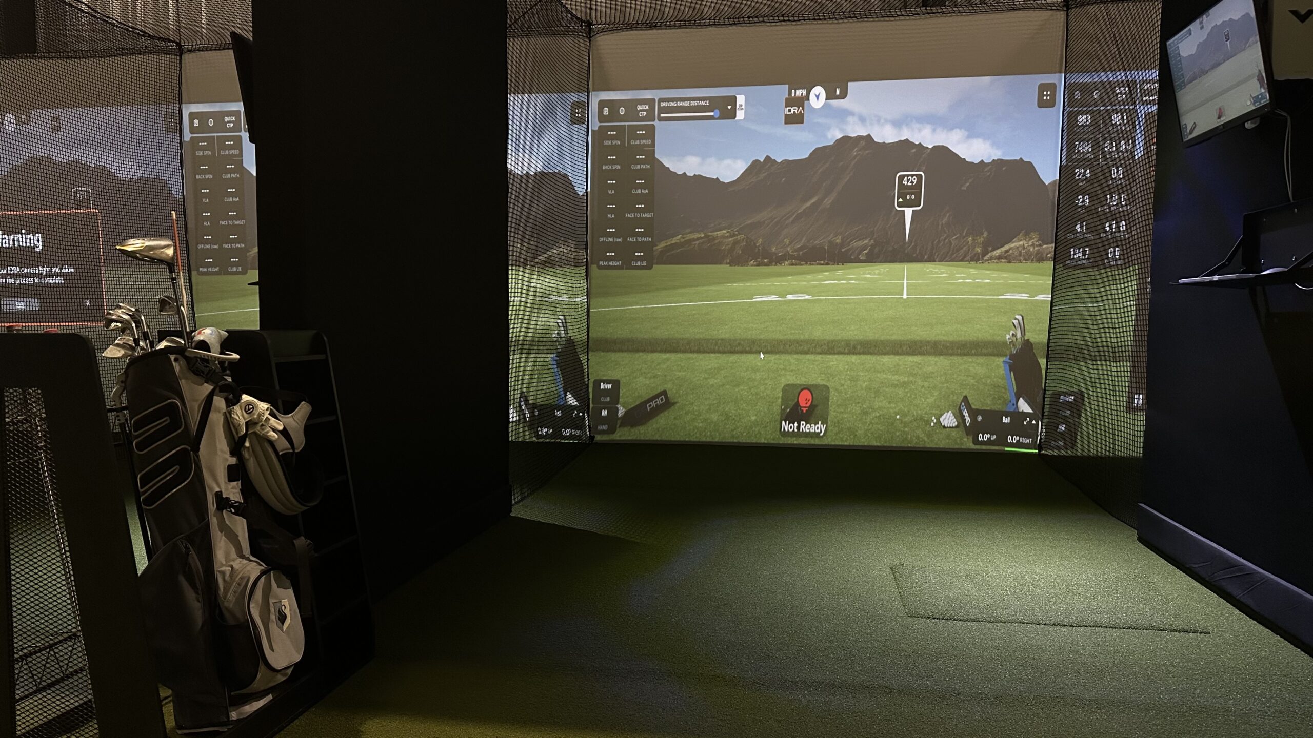 A golf simulator setup with a projected screen displaying a virtual course, golf clubs in a bag, and artificial turf flooring—perfect for practicing your swing or making golf reservations through Tee24.